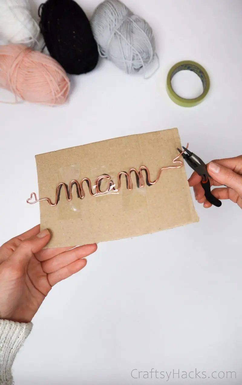 bending wire with pliers to spell name on cardboard
